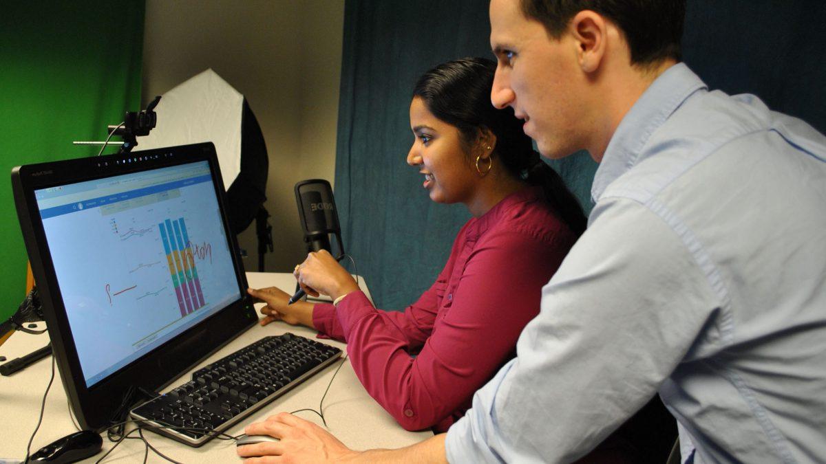 Two students working and looking at a computer.